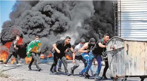  ?? AFP ?? Jóvenes palestinos empujan un contenedor utilizado como barricada en el sur de Nablus, en Cisjordani­a