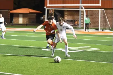  ?? Photo by Kevin Sutton ?? Texas High striker Austin Miller, No. 22, fights for possession with Pleasant Grove’s Peyton Legrand, No. 18. Miller had four goals for the Tigers, who beat the Hawks 6-0 on a windy night at Tigers Stadium at Grim Park in Texarkana.