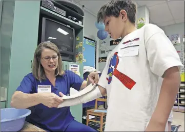  ?? AUSTIN AMERICAN-STATESMAN FILE PHOTO ?? During science day at Bridgeport Elementary School in Texas, Charles Sansbury gets to experience what it’s like to wear a cast as Dr. Melanie Collins wraps his arm in one. Injuries leading to broken bones are more common in the summer for kids in early elementary school.