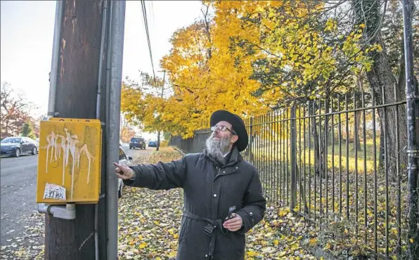  ?? Andrew Rush/Post-Gazette photos ?? Rabbi Shimon Silver inspects a plastic casing attached to a utility pole designatin­g the perimeter of the Pittsburgh eruv on Thursday in Squirrel Hill. Rabbi Silver spends every Thursday morning driving and walking the perimeter of the eruv, a kind of wall designated by utility poles and natural features that allows Orthodox Jews to carry things on the Sabbath.