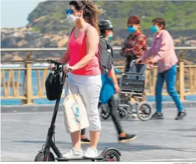  ?? JUAN HERRERO / EFE ?? Una mujer en un patinete eléctrico protegida con una mascarilla por el paseo de la Zurriola de San Sebastián.