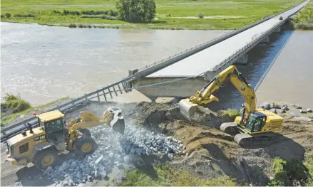  ?? RICK BOWMER/AP ?? Highway workers build up the shoreline under a washed-out bridge along the Yellowston­e River on June 15 near Gardiner, Montana.