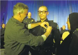  ?? PATRICK TEHAN/STAFF ?? Ziad Salman, left, pins a badge on his son, Tarik Awwad, as Awaad's mother, Fatmeh Mustafa, looks on, during the graduation of the San Jose Police Department’s Academy 28.