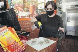  ?? Myung J. Chun Los Angeles Times ?? AT EL TARASCO, a Mexican food joint in Marina del Rey, cashier Maricela Moreno takes each banknote offered to her and sprays it down with alcohol.