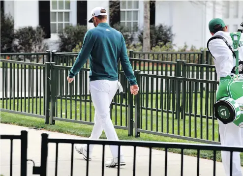  ?? BRANT SANDERLIN / THE ASSOCIATED PRESS ?? Dustin Johnson walks off the first tee Thursday after deciding not to play in the opening round of the Masters because of a back injury.