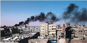  ?? Photo: AFP ?? A man on a rooftop takes photos of smoke rising after an Israeli bombing raid in Rafah.