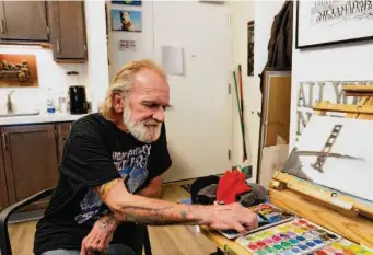  ?? ?? Army veteran Randall Larson, a longtime artist partially paralyzed in an accident, looks over his paints in his apartment at the complex. “I don’t know where I’d be if not for this place,” he says.