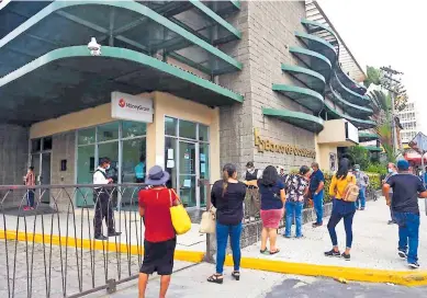  ??  ?? CLIENTES. Varias personas hacen fila afuera de una agencia bancaria de San Pedro Sula.