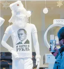  ??  ?? Bright side: A man takes pictures of a shop mannequin in Russia that displays a T-shirt reading: ‘‘In rouble I trust’’.