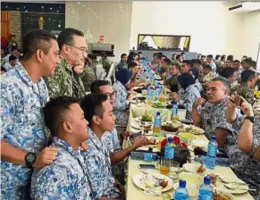  ??  ?? Hearty meal: Hishammudd­in (standing second from left) having a chat with officers at the Lok Kawi army camp.