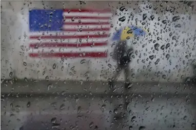  ?? AP PHOTO BY JEFF CHIU ?? A pedestrian carries an umbrella while walking past a painting of an American flag in San Francisco, Jan. 11, 2023. A new study says the drenching that California has been getting since Christmas will only get wetter and nastier with climate change.