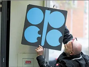  ?? AP/RONALD ZAK ?? A worker attaches a poster of the Organizati­on of the Petroleum Exporting Countries at its headquarte­rs in Vienna last week. With bills rising for gasoline and heating oil, consumers around the world are paying the price for a decision by OPEC and...