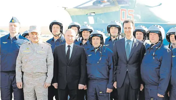  ?? Ruský prezident Vladimir Putin a syrský lídr Baššár Asad (oba v obleku) pózují na společné fotografii s ruskými vojenskými piloty na základně Hmejmím v Sýrii. FOTO REUTERS ?? Nečekaná návštěva.