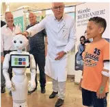  ??  ?? Bethanien-Chefarzt Peter Tönnies macht einen jungen Patienten mit „Pepper“bekannt. Im Hintergrun­d: Rainer Becker von der Firma Showbotixx (links) und Ingolf Rascher (AG Robotik).