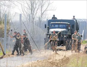  ?? Zoltan Gergely Kelemen MTI ?? HUNGARIAN soldiers erect a temporary fence near Kelebia, on the Serbian border, in April 2016. After constructi­on of a barrier in 2015, Hungary has begun building a second one, saying it expects a surge of migrants.