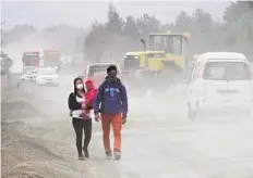  ?? Reuters ?? Volcanic ash Residents protect themselves against ash from Calbuco volcano on a street in Ensenada as a wheel loader moves piles of volcanic ash to the roadside.