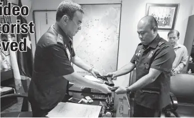  ??  ?? DISARMED COP — Chief Inspector Melvin Madrona (right) surrenders his service firearm to Chief Superinten­dent Guillermo Eleazar, Quezon City Police District (QCPD) director, yesterday at Camp Karingal before submitting himself to restrictiv­e custody of...