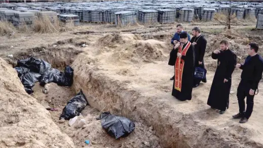  ?? RONALDO SCHEMIDT/AFP VIA GETTY IMAGES ?? Priests pray over body bags in a mass grave on Thursday at St. Andrew Church in Bucha, Ukraine.