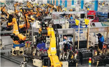  ?? — THE ASSOCIATED PRESS FILES ?? Workers assemble parts next to robot arms in a factory. Workers should be learning new skills, a Business Council of B.C. analysis says