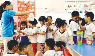  ??  ?? A kindergart­en teacher helping some of her charges to apply disinfecta­nt in the wake of the HFMD outbreak in Kuala Lumpur yesterday.