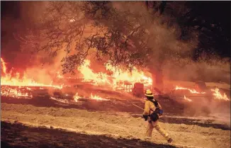  ?? Noah Berger / Associated Press ?? A firefighte­r passes flames while battling the Glass Fire in a Calistoga, Calif., vineyard on Thursday.