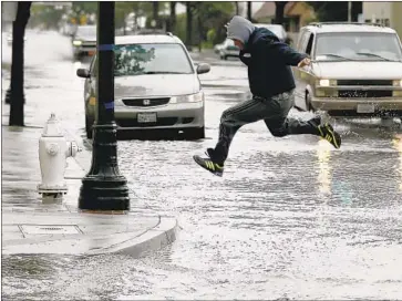  ?? Allen J. Schaben Los Angeles Times ?? A PEDESTRIAN takes flight crossing Fourth Street in Santa Ana after heavy rains flooded the area in 2017. California has warmed 1 to 2 degrees Fahrenheit since 1900, making storms more powerful, scientists say.