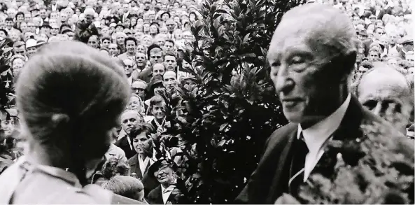  ??  ?? Ein Mädchen aus Emmerich übergibt Konrad Adenauer auf der Rathaustre­ppe Blumen. Dahinter ist der Platz voll mit Menschen.