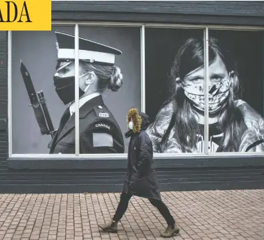  ?? PETER J THOMPSON/NATIONAL POST ?? A pedestrian wearing a mask walks past photos by photograph­ers Dave Chan, left, and Jennifer Long
at a Toronto exhibit called Portraits In Covid Times: Documentin­g A Nation In Change.