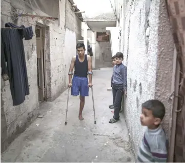  ??  ?? Al-Ajouri, 17, stands on crutches Apr 18, outside his family home in the Jabalya refugee camp in the northern Gaza Strip. His leg was struck by an Israeli soldier’s bullet amid recent demonstrat­ions along the Gaza border.