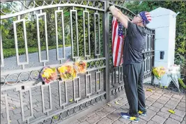  ?? Marta Lavandier The Associated Press ?? John Hensel attaches an American flag to the gate of the home of his friend, talk radio host Rush Limbaugh, who died Wednesday in Palm Beach, Fla. Limbaugh, 70, revealed a year ago that he had lung cancer.