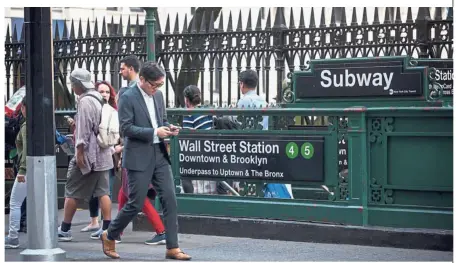  ?? — Bloomberg ?? Downtrend: A pedestrian viewing a mobile device while walking past the Wall Street subway station in New York on Friday. Most US equities drifted lower as global stocks lost momentum, with European and Asian peers retreating.