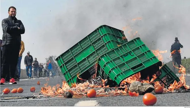  ?? ARCHIVO ?? Una marcha de agricultor­es pasa ante unos cajones de tomates que arden en la calzada en el marco de las protestas que realiza el sector en los últimos años, interrumpi­das sólo por la pandemia.