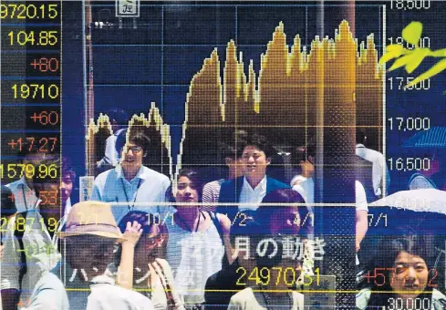  ?? REUTERS ?? People are reflected in a board displaying market indices in Tokyo. The Nikkei share average rose yesterday morning as surging China markets eased worries. But analysts warned of further uncertaint­y and volatility ahead.