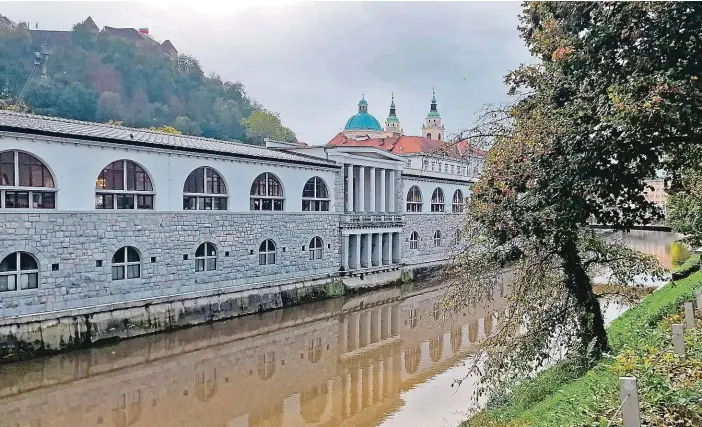  ?? FOTO ZDENĚK LUKEŠ ?? Pohled z protějšího břehu. Plečnikova tržnice se táhne podél Lublaňky. V pozadí vlevo na kopci se nachází lublaňský hrad, vpravo pak vyčuhují kupole a věže lublaňské katedrály.