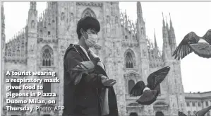  ?? Photo: AFP ?? A tourist wearing a respirator­y mask gives food to pigeons in Piazza Duomo Milan, on Thursday.