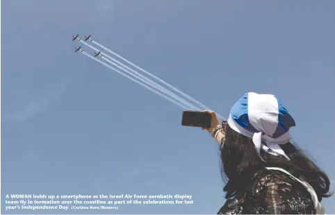  ?? ?? A WOMAN holds up a smartphone as the Israel Air Force aerobatic display team fly in formation over the coastline as part of the celebratio­ns for last year’s Independen­ce Day. (Corinna Kern/Reuters)