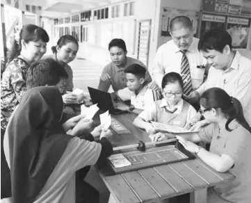  ??  ?? (Standing from right) Ting, Ng and Bong (left) helping the students prepare flyers for distributi­on to the public.