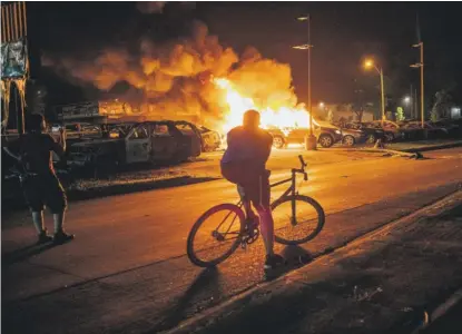 ?? BRANDON BELL/GETTY IMAGES ?? People watch a used-car lot burn Aug. 24 in Kenosha, Wisconsin.