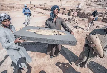  ?? KHALED DESOUKI/GETTY-AFP ?? Workers carry a fish covered in gold Saturday at the archaeolog­ical site of the remains a 3,000-year-old city near Luxor, Egypt. Archaeolog­ist Zahi Hawass said brick houses, artifacts and tools were found. The city dates back to Amenhotep III of the 18th dynasty, whose reign is considered a golden era for ancient Egypt.