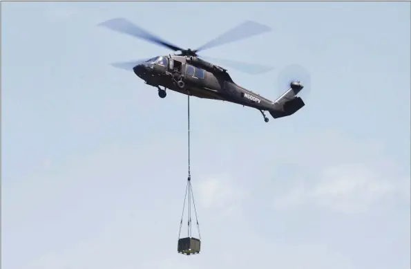  ?? Ned Gerard / Hearst Connecticu­t Media ?? A Sikorsky UH-60A Black Hawk helicopter hovers with a payload at Sikorsky Memorial Airport in Stratford, July 13. Sikorsky uses the helicopter for test flights for a new Aircrew Labor In-Cockpit Automation System (ALIAS), a fly-by-wire system that will allow it to be flown with no people aboard.