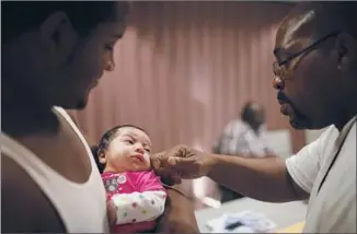  ??  ?? VINCENT McGRUDER, left, holds his baby son, Vincent Jr., during a Project Fatherhood meeting at Jordan Downs. Willie Charles Freeman, right, gets acquainted with the little guy.