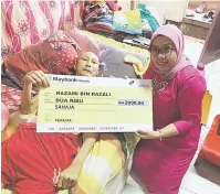  ??  ?? BANTU: Siti Aisyah (kanan) menyampaik­an replika cek kepada Razami pada kunjungan pihak yayasan di kediaman Razami di Kuching, semalam