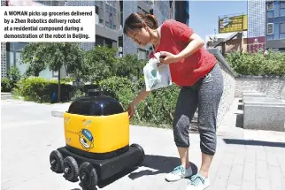  ??  ?? A WOMAN picks up groceries delivered by a Zhen Robotics delivery robot at a residentia­l compound during a demonstrat­ion of the robot in Beijing.