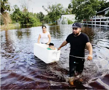  ?? Foto: David Goldman/AP/dpa ?? Mit einer Kühlbox ziehen diese Eltern in Bonita Springs (USA) über eine überflutet­e Straße.