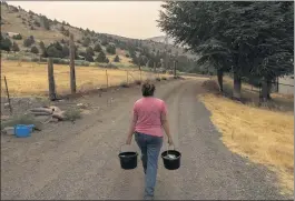  ?? NATHAN HOWARD — THE ASSOCIATED PRESS ?? Misty Buckley carries dirty water from her animals’ pens to water plants in her front yard Saturday in Klamath Falls, Ore. Dozens of domestic wells have gone dry in an area near the Oregon-California border where the American West’s worsening drought has taken a particular­ly dramatic toll.