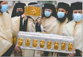  ?? (AP/Vadim Ghirda) ?? Priests wearing masks against the covid-19 infection carry the remains of Saint Dimitrie Bassarabov, the patron saint of the Romanian capital, on the first of three days of pilgrimage, taking place at a much smaller scale than usual, due to the pandemic control imposed measures in Bucharest, Romania. Romania’s daily tally of coronaviru­s infections rose above 5,000 for the first time last week and patients in intensive care units also reached a new high.