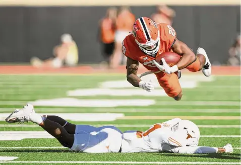  ?? Brody Schmidt/Associated Press ?? Oklahoma State's Dominic Richardson leaps over Texas defensive back Anthony Cook during the first half Saturday in Stillwater, Okla.