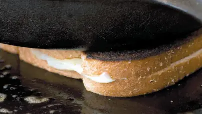  ?? AP FILE PHOTO ?? A cast iron pan is used to weigh down a grilled cheese sandwich as it cooks on a skillet. A Quebec coroner has warned the popular sandwich is a danger for elderly people, after two seniors in the province choked to death on them.