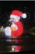  ?? (AP/Gregorio Borgia) ?? Rain drops on a car window are backdroppe­d by city lights and a giant lighted figure of Santa Claus on Dec. 9 in Naples, Italy.