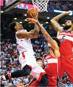  ?? (Reuters) ?? TORONTO RAPTORS guard DeMar DeRozan (left) drives to the basket over Washington Wizards defenders Kelly Oubre Jr. and Markieff Morris (5) for two of his game-high 32 points in the Raptors’ 108-98 home victory over the Wizards on Wednesday night to take...